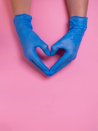 Doctor hands in blue disposable medical gloves in heart shape on pink background. Love and compassion. Hygiene to prevent Covid-19 virus, successful heart disease treatment and coronavirus protectionの写真素材