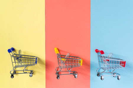 Empty supermarket shopping trolley cart on colorful yellow, red and blue background. Shopping,...