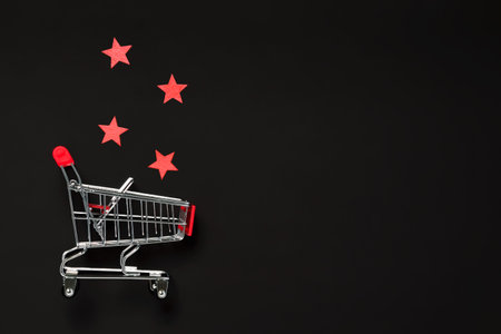 Black Friday sale concept. Shopping cart and red stars on dark background. Holiday shopping for...