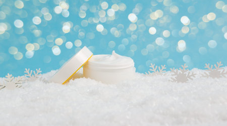 Opened face cream jar and snowflakes in snow on blue background with bokeh lights. Moisturizing hand creme, face mask or body lotion. Winter skin care cosmetic products. Seasonal weather protectionの写真素材