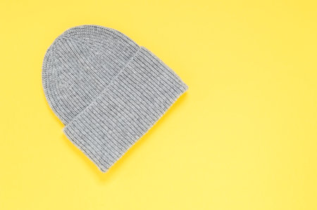 Grey knit cap on yellow background. Fashionable warm autumn and winter accessory. Trendy colors of year 2021 illuminating yellow and ultimate gray and copy space for textの写真素材