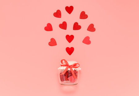Red wooden hearts in jar with bow knot on pink pastel background. Romantic heart composition for Valentines day or mothers day card. Give and preserve love concept.の写真素材