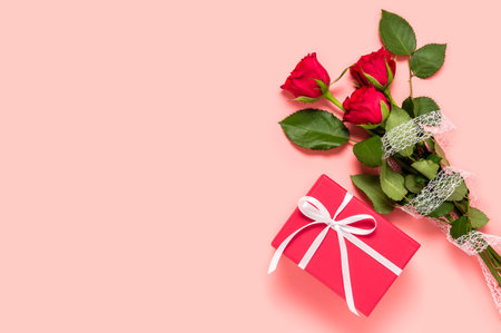 Bouquet of three red roses and gift box on pink background. Birthday, Mother's, women's or Valentine's day greeting. Love and dating concept. Flat lay with copy space for text on left sideの写真素材