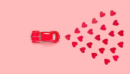 Fulda, Germany - DEC 18, 2020: Red retro toy car with many red hearts for Valentines day on pink...