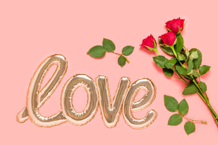 Golden foil balloon in shape of Love word and three red roses bouquet on pink background. Love and dating concept. Mothers, Valentines day or wedding celebration. Top view, flat layの写真素材