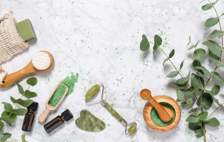Natural skin care and aromatherapy with eucalyptus essential oil bottle, bath salt, beauty jade roller, gua sha on marble background. Spa, wellness, massage, relaxation concept. Top view, copy spaceの写真素材