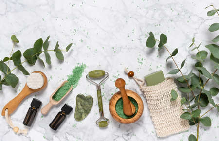 Natural skin care and aromatherapy with eucalyptus essential oil bottle, bath salt, beauty jade roller, gua sha on marble background. Spa, wellness, massage, relaxation concept. Top view, copy spaceの写真素材