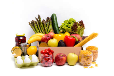 Cardboard box with fresh fruit and vegetables, eggs, pasta and canned food. Donation or food delivery concept. Vegetarian grocery products, isolated on white background.の写真素材