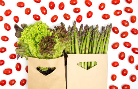 Green and red vegetables - lettuce, asparagus and cherry tomatoes isolated on white background. Healthy diet, vegetarian products, grocery shopping, donation or food delivery concept. Top view.の写真素材