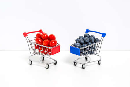 Blueberries and cherry or roma tomatoes in shopping carts isolated on white background. Shopping for berries, healthy diet and natural vitamin foodの写真素材