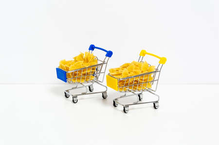 Uncooked farfalle pasta in blue and yellow shopping carts in colors of Ukrainian flag isolated on white background. Food supply crisis, price increase for wheat products, groceries shopping conceptの写真素材