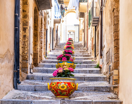 Narrow street in the old town of Cefalu, medieval village on Sicily island, Italy. Flower pots with traditional sicilian decoration. La Rocca cliff. Popular tourist attraction in Province of Palermoの写真素材