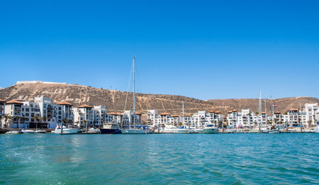 Seaside view of Agadir Marina in Morocco. Popular tourist area with luxury apartments, boats in harbor, shops and restaurants. Moroccan seaside resort on shore of Atlantic ocean in Africa.の写真素材