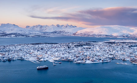 Aerial view of Tromso, Norway at sunset in winter from Storsteinen mountain. Tromsoya island with snowy roofs of Tromso downtown, harbor, cruise ship in fjord water and mountains in background.の写真素材