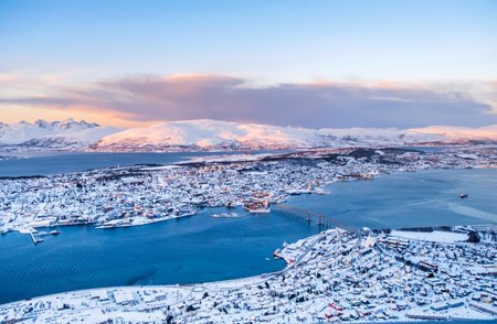 Aerial view of Tromso, Norway at sunset in winter from Storsteinen mountain. Tromsoya island with snowy roofs of Tromso downtown, harbor, Sandnessundet Bridge over Fjord and mountains in background.の写真素材