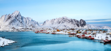Reine village with traditional rorbu houses on Lofoten islands in winter. Scandinavian landscape with red wooden fishermen cabins on fjord water and snowy mountains, northern Norwayの写真素材