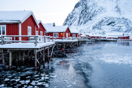 Reine village with traditional rorbu houses on Lofoten islands in winter. Scandinavian landscape with red wooden fishermen cabins on frozen sea water and snowy Reinebringen mountain in northern Norwayの写真素材