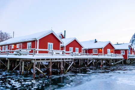 Reine village with traditional rorbu houses on Lofoten islands in winter. Scandinavian landscape with red wooden fishermen cabins on frozen fjord water, northern Norwayの写真素材