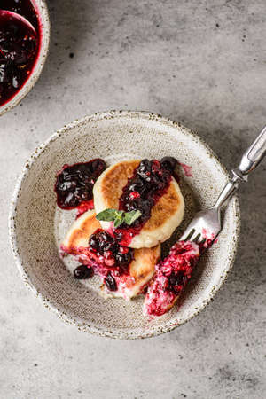 vegetarian vegetarian cottage cheese cake with black currant jam in the gray bowl on gray background. No eggs with banana. A bowl of jam is nearby. top view, close-upの写真素材