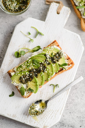 avocado toast with pesto sauce. bread lies on a white board, sprinkled with sesame seeds next to...