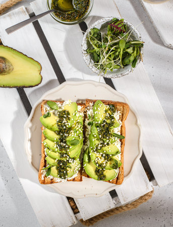 avocado toast with pesto sauce. the bread is on a white wooden tray, sprinkled with sesame seeds...