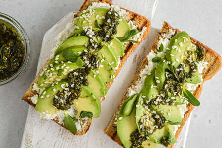 avocado toast with pesto sauce. bread lies on a white board, sprinkled with sesame seeds next to pesto sauceの写真素材