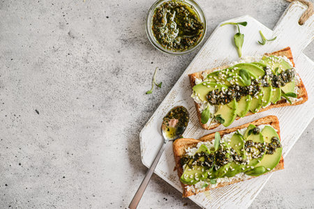 avocado toast with pesto sauce. bread lies on a white board, sprinkled with sesame seeds next to...
