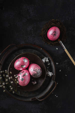 painted easter eggs on a black tray. The eggs are painted pink and decorated with enamel and sequinsの写真素材