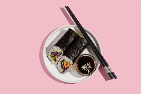A rice roll with vegetables in seaweed lies on a plate with soy sauce