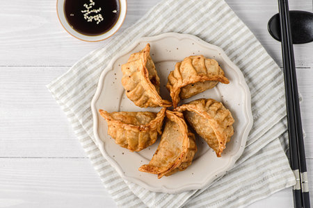 gyoza with stuffing and soy sauce. assorted gyoza are on a plate, next to soy sauce and sushi sticks