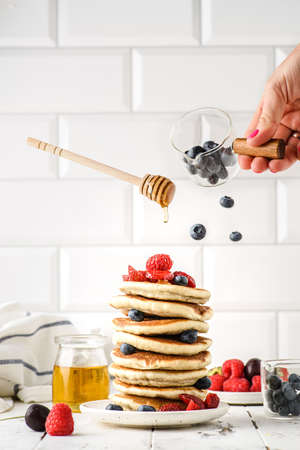 stack of pancakes with berries levitation. Nearby there is a jar of honey, bowls with blueberries and raspberries, a honey spoon levitatingの写真素材