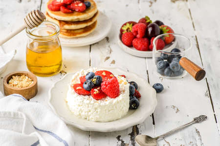 cottage cheese with raspberries, strawberries and blueberries. Cottage cheese is laid out in the form of a pastry ring, next to a jar of honey and chopped nuts. Often eaten for breakfast in Russiaの写真素材