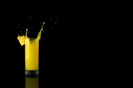 pineapple juice in a glass on a black background with reflection with splashes and splashes. high quality photoの写真素材