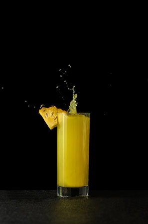 pineapple juice in a glass on a black background with reflection with splashes and splashes. high quality photoの写真素材