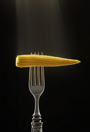 mini corn on a fork with steam on black background. high quality photo