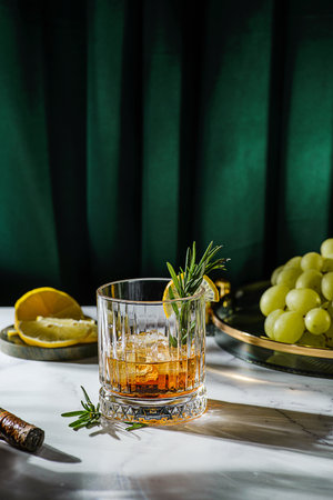 a glass of whiskey on the table is decorated with lemon and rosemary, There are grapes on a tray nearbyの写真素材