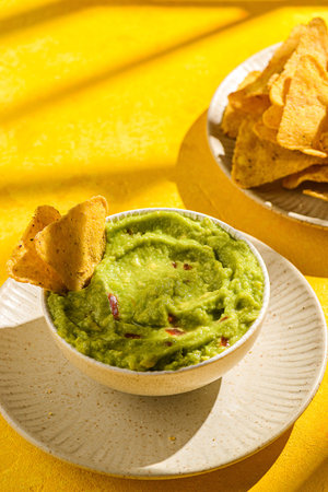 nachos with avocado guacamole on a yellow background. Guacamole is a traditional Mexican snack made...