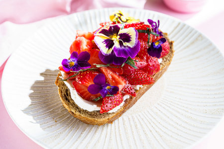 bruschetta with strawberries and cream cheese, decorated with viola flowers and sprinkled with...