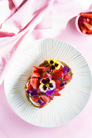 bruschetta with strawberries and cream cheese, decorated with viola flowers and sprinkled with...