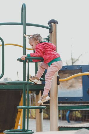 A child on the Playground with a cute face on a natural background. A little girl with blond hair pulled back in ponytails. Beauty, dexterity, hairstyle. The concept of a happy childhood.の写真素材