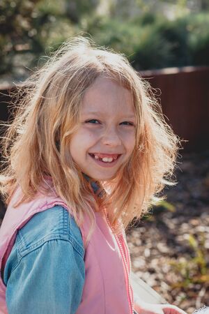 a cute girl with disheveled hair on a Sunny day is laughing and smiling. natural beauty, a delicate girl's face, naturalness, a teenager, a daughter stands on the street in the spring. European child in a blooming Park, the concept of a happy childhoodの写真素材