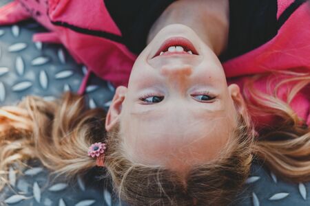 Child with smile on cute face on natural background. Little girl with blond hair ponytails smiling outdoor. Beauty, look, hairstyle. Happy childhood concept.の写真素材