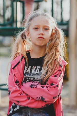 A child on the Playground, offended, cute face on a natural background. A little girl with blond hair pulled back in ponytails. The beauty, the emotion, the hair. The concept of a happy childhood.の写真素材