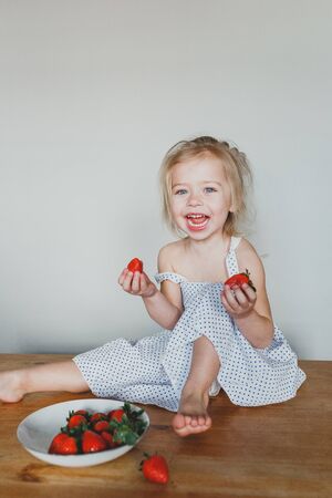 cute European girl eating strawberries. a beautiful, cheerful blonde with blue eyes.の写真素材