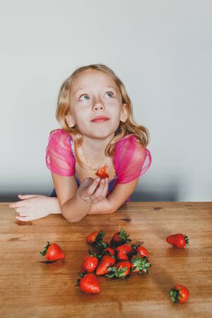 cute European girl eating strawberries. a beautiful, cheerful blonde with blue eyes.の写真素材