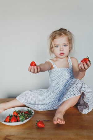 cute European girl eating strawberries. a beautiful, cheerful blonde with blue eyes.の写真素材