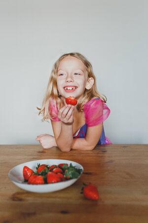 cute European girl eating strawberries. a beautiful, cheerful blonde with blue eyes.の写真素材