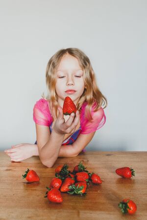 cute European girl eating strawberries. a beautiful, cheerful blonde with blue eyes.の写真素材