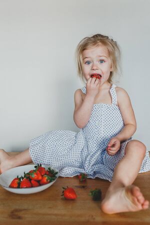 cute European girl eating strawberries. a beautiful, cheerful blonde with blue eyes.の写真素材