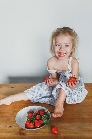 cute European girl eating strawberries. a beautiful, cheerful blonde with blue eyes.の写真素材
